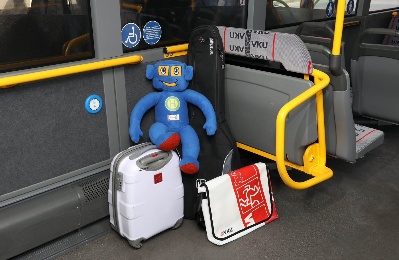 Nimbu, das Maskottchen der Busschule NimmBus sitzt auf Koffern in einem Bus.