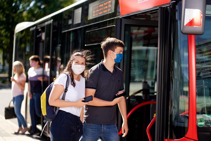 Menschen steigen mit Mund-Nasen-Bedeckung in einen Bus ein.