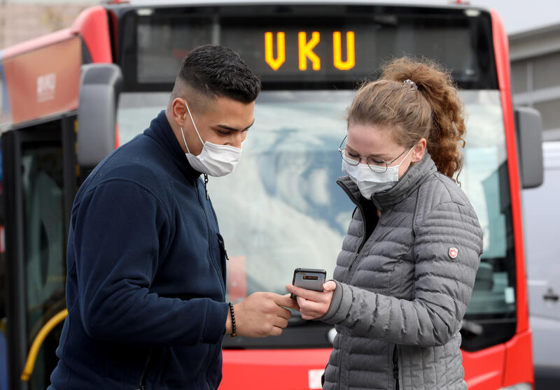 Ein Mann und eine Frau mit Mund-Nasen-Schutz, schauen auf ein Smartphone.